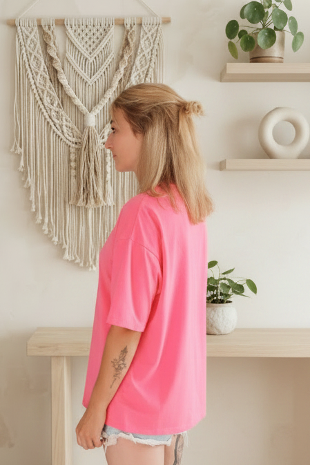 Boho-Luxe Look: Frau in leuchtend pinkem Baumwoll-T-Shirt vor Makramee-Wanddeko.