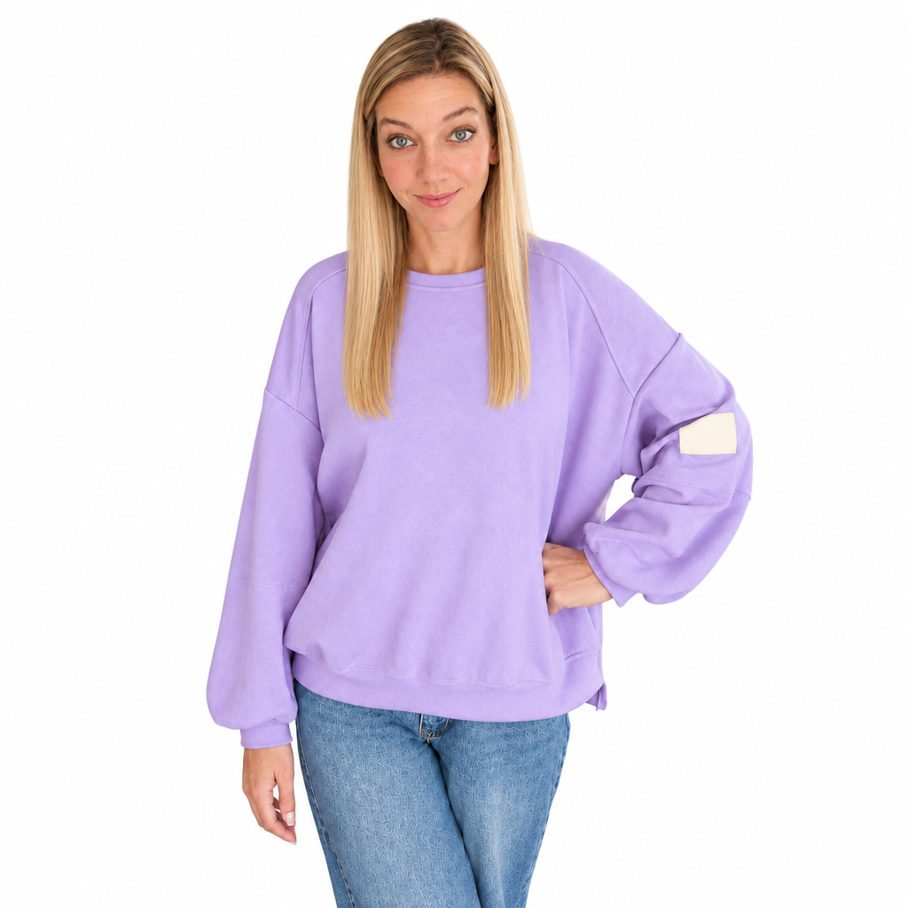 Fliederfarbenes Damen-Sweatshirt mit Rundhalsausschnitt, weiten Ärmeln und hellem Ärmelpatch, am Model zur blauen Jeans vor weißem Hintergrund.