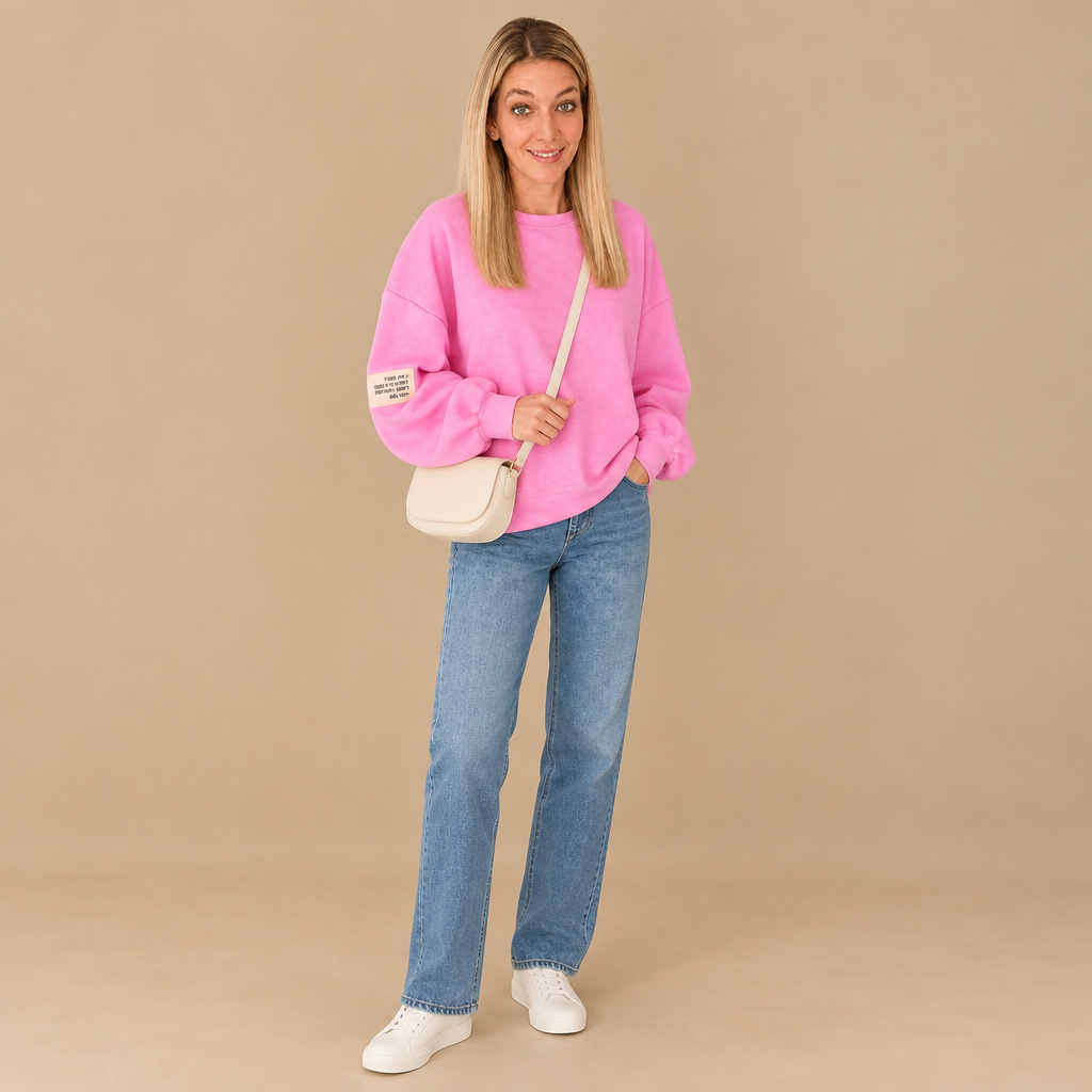 Damen-Outfit mit pinkem Sweatshirt, blauer Straight-Leg-Jeans, weißen Sneakern und cremefarbener Umhängetasche.