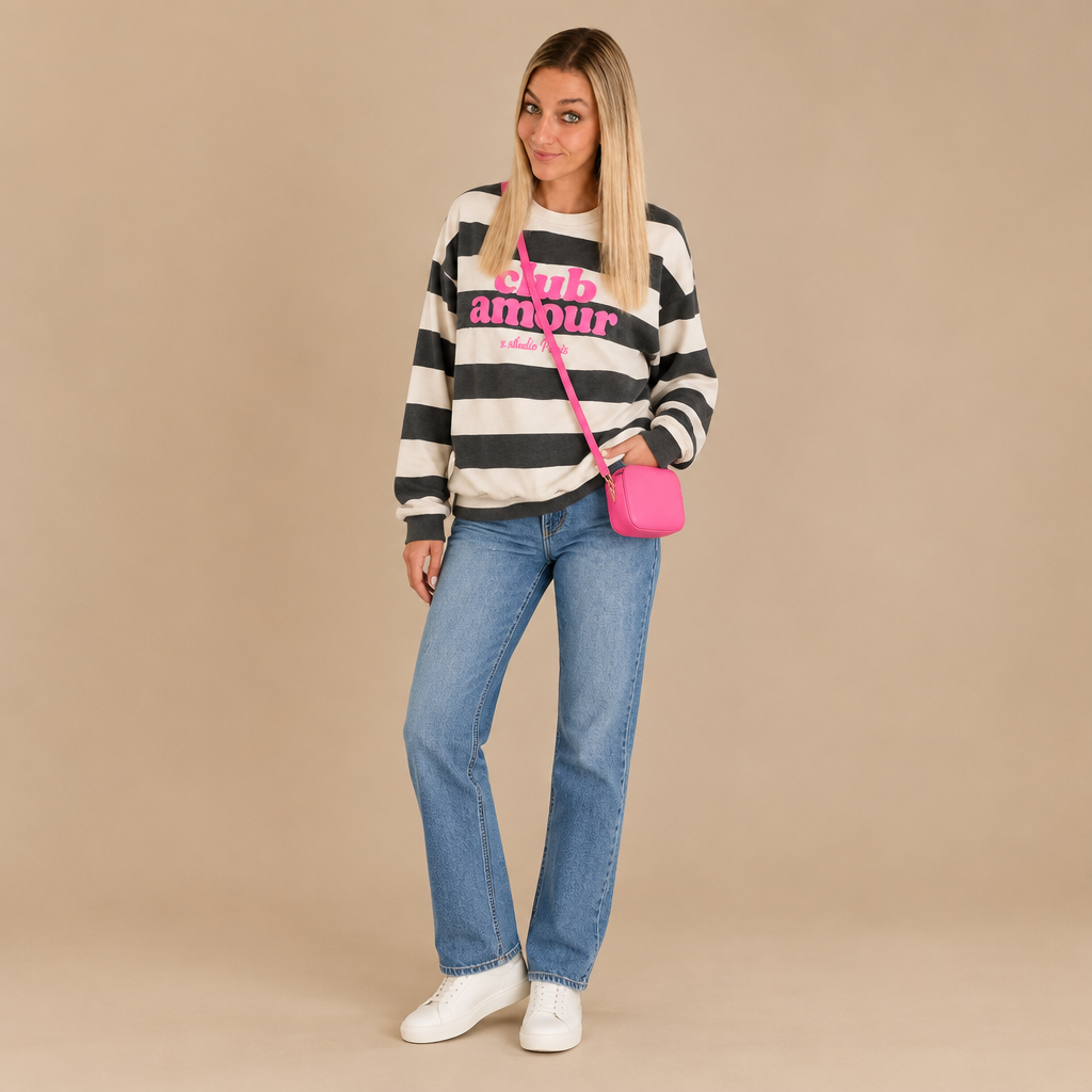 Damen-Outfit mit gestreiftem Club-Amour-Sweatshirt, blauer Straight-Leg-Jeans, weißen Sneakern und pinker Umhängetasche.