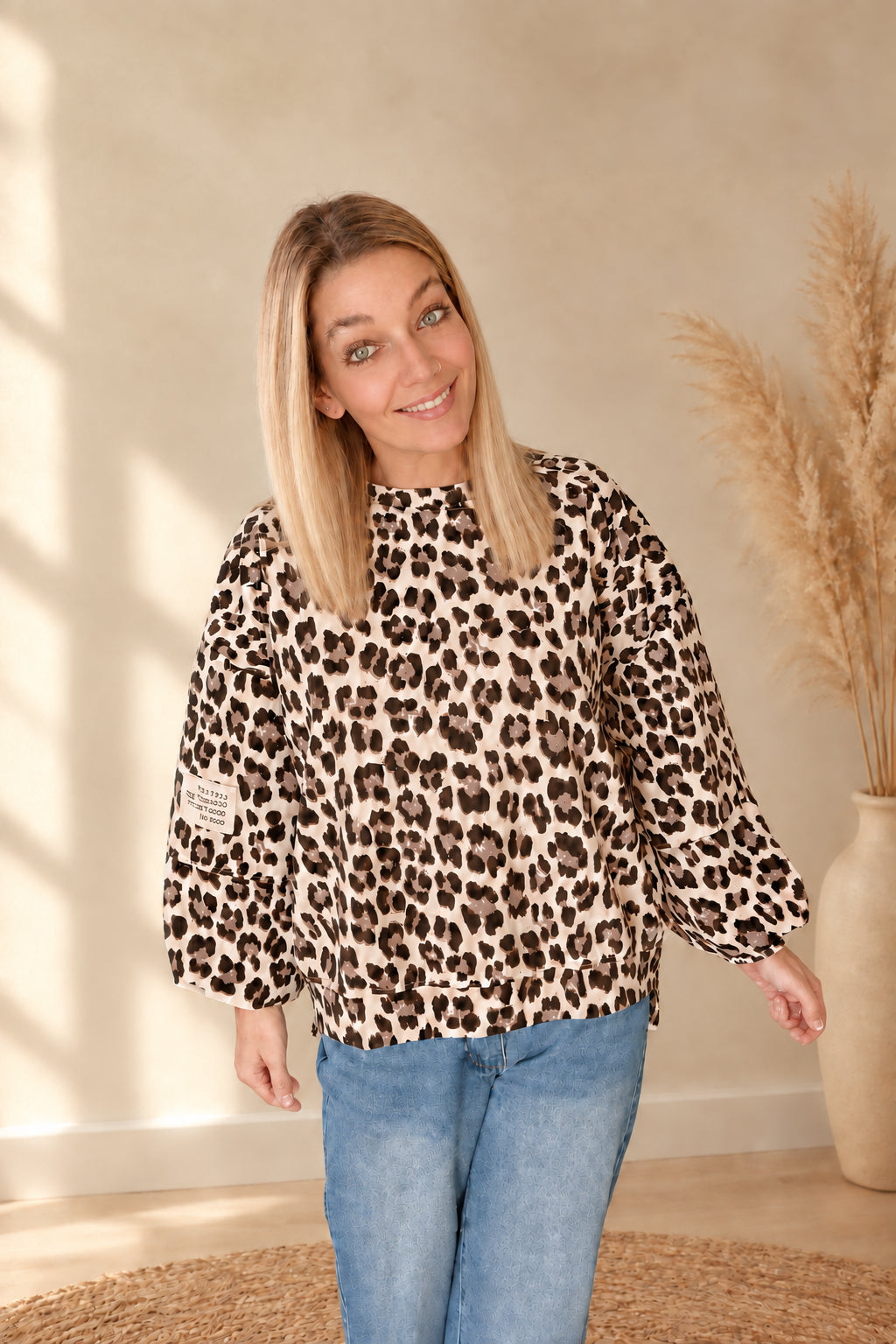 Damen-Oberteil mit Leoprint und Ärmelpatch, am lächelnden Model mit gesenkten Armen zur blauen Jeans.
