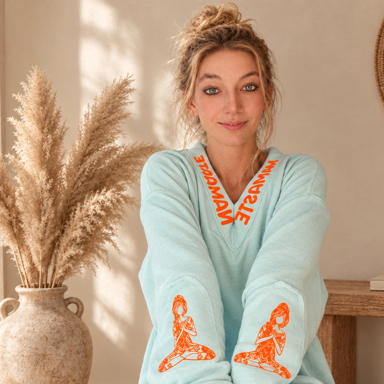 Mintfarbener Damenpullover mit orangefarbenen Motiven auf beiden Ärmeln, Detailansicht am Model