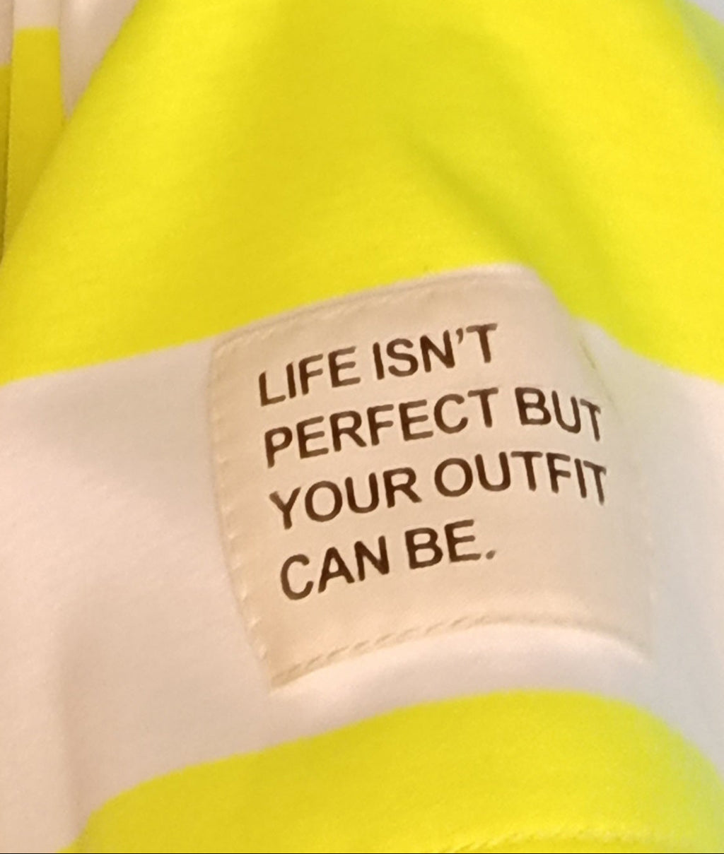 Gelbes Textil mit weißem Label und dem Spruch 'Life isn't perfect but your outfit can be'.