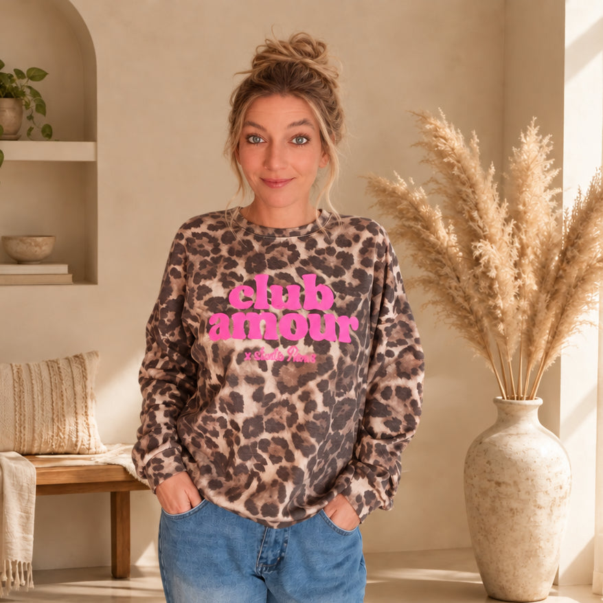 Pullover mit Leo-Print in Beige und Braun und pinkem Schriftzug, frontal am Model mit den Händen in den Hosentaschen.