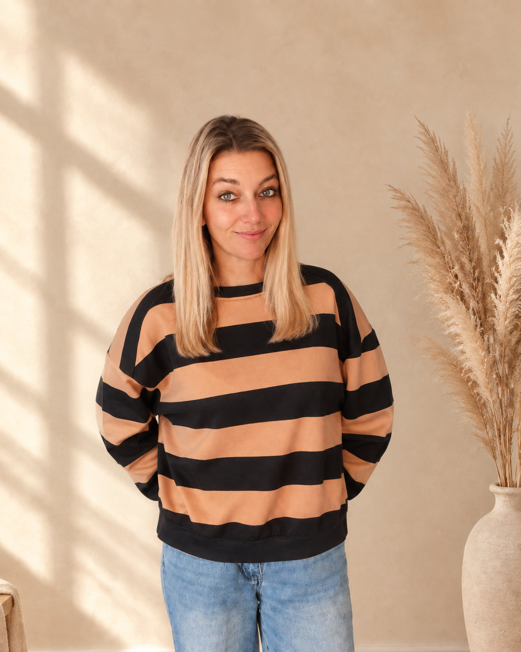 Vorderansicht des camel-schwarz gestreiften Damen-Sweatshirts, am Model mit Händen hinter dem Rücken.