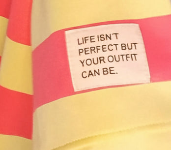 Boho-Luxe Detail: Weißes Etikett mit Spruch auf gelb-pink gestreiftem Stoff.