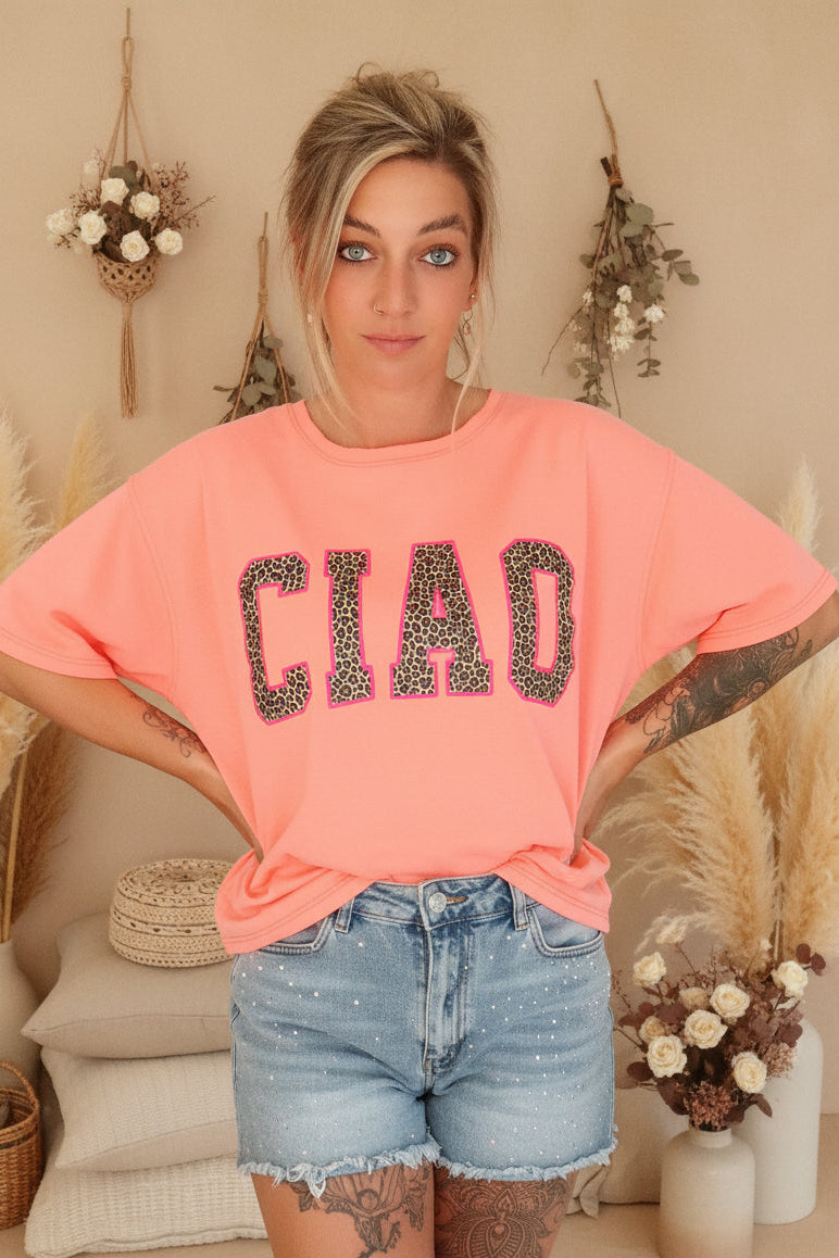 Boho-Luxe Style: Korallenfarbenes T-Shirt mit Leopardenprint-Schriftzug und Denim-Shorts.