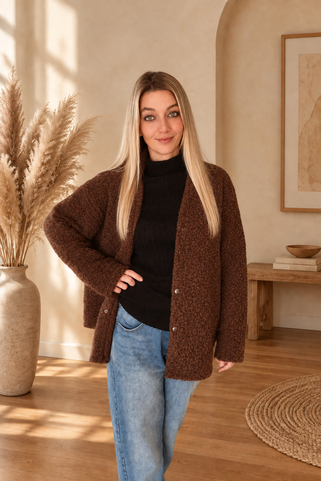 Braune Damenjacke mit strukturierter Oberfläche, offen über schwarzem Oberteil getragen, eine Hand an der Hüfte.