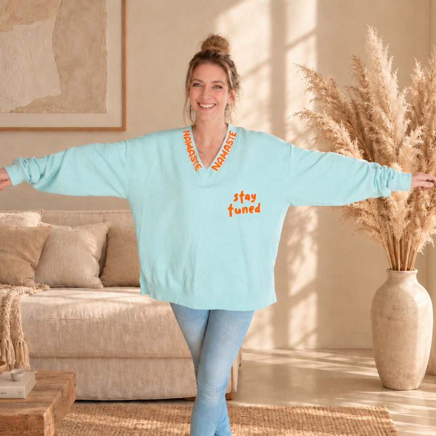 Weit geschnittener mintfarbener Damenpullover mit V-Ausschnitt und orangefarbenen Prints, Ansicht mit ausgestreckten Armen