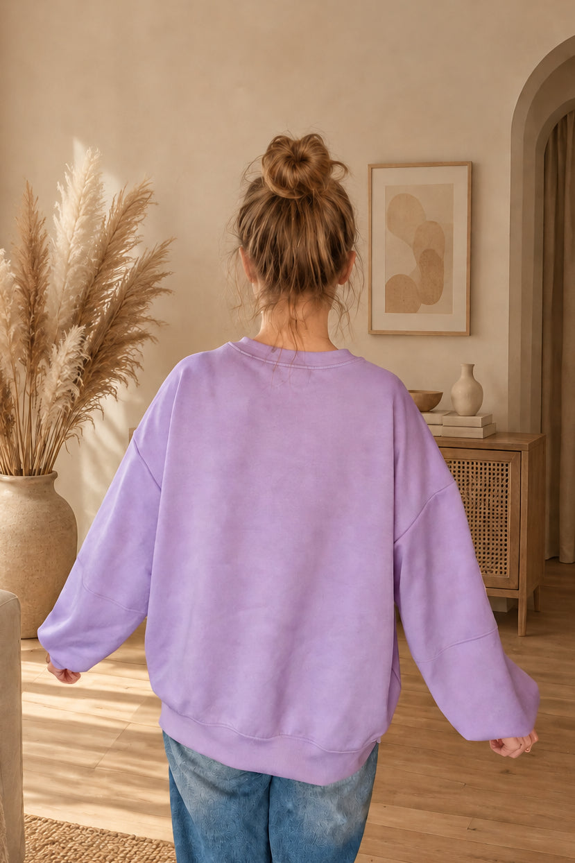Rückansicht des fliederfarbenen Damen-Sweatshirts mit lockerem Schnitt und Saumbündchen, am Model mit Dutt und leicht ausgestreckten Armen.