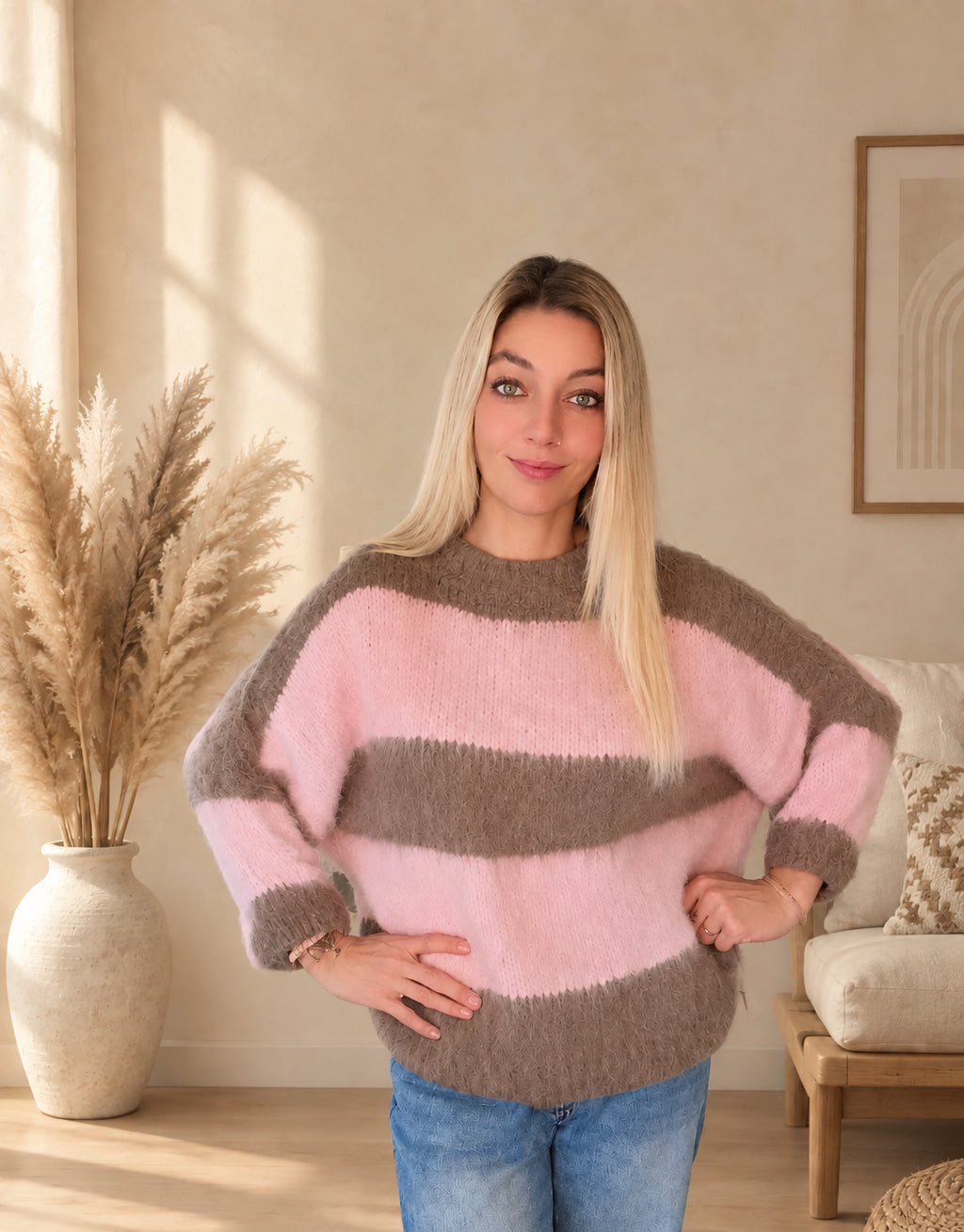 Frontansicht des Damen-Strickpullovers mit breiten rosa-braunen Streifen, am Model mit beiden Händen an den Hüften.