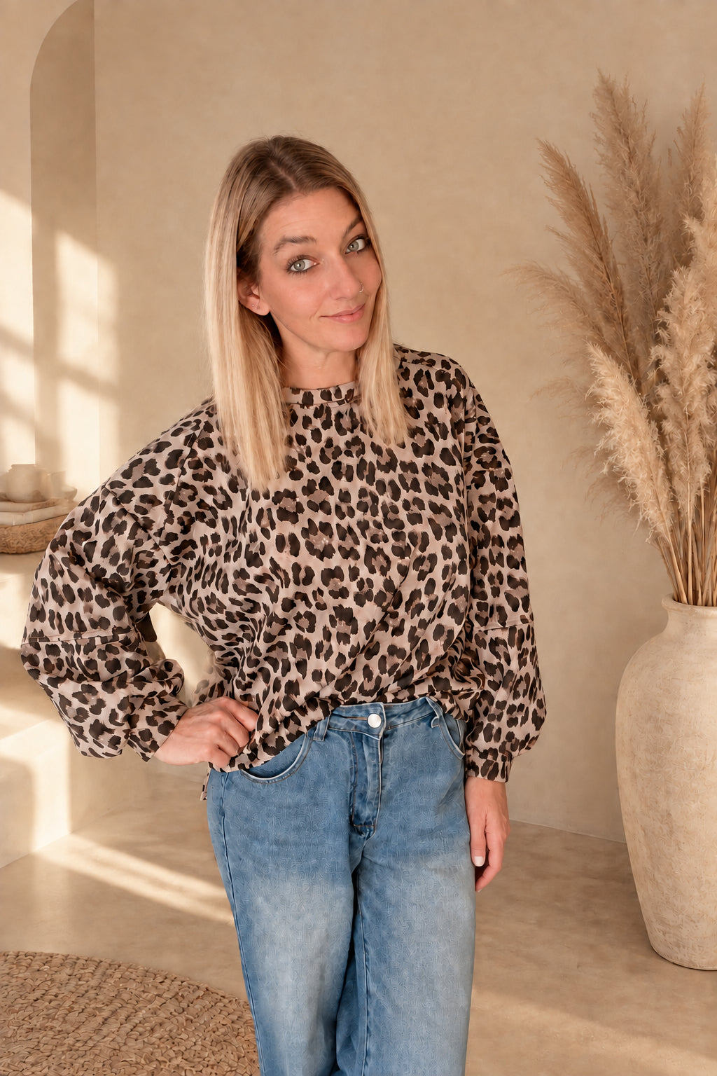 Damen-Oberteil mit Leoprint, vorne in eine blaue Jeans gesteckt, am Model mit einer Hand an der Hüfte.