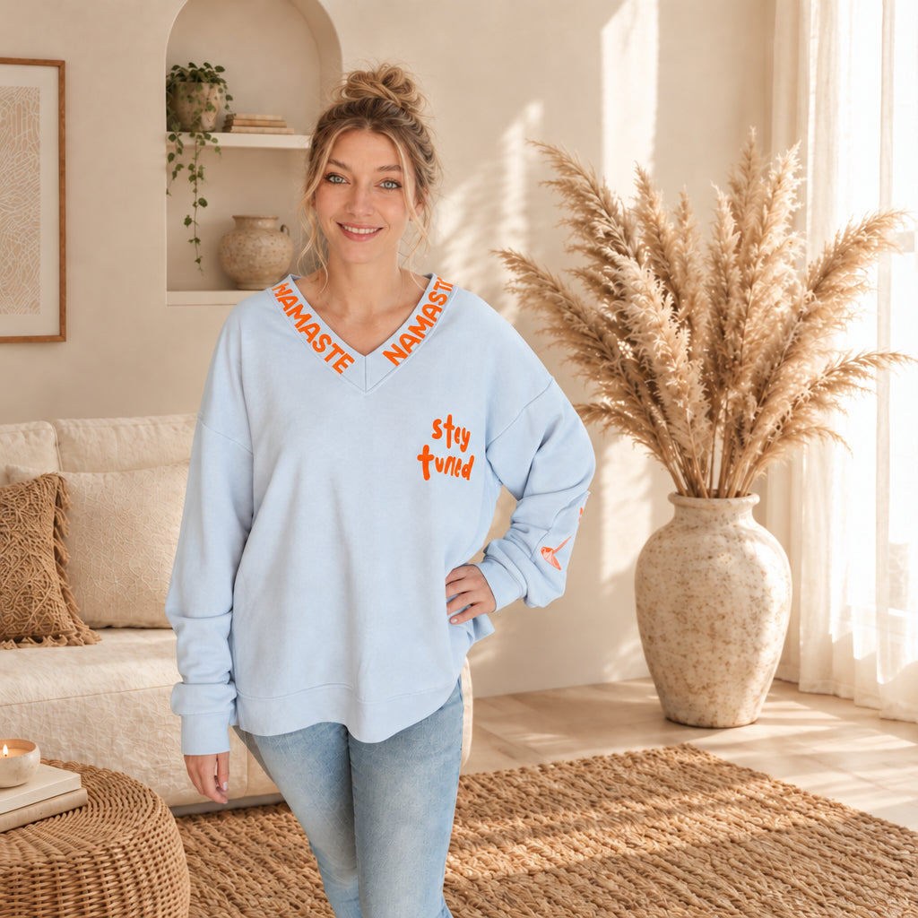 Hellblauer Damenpullover mit orangefarbenem Namaste-Schriftzug am V-Ausschnitt und „stay tuned“-Print, Frontansicht