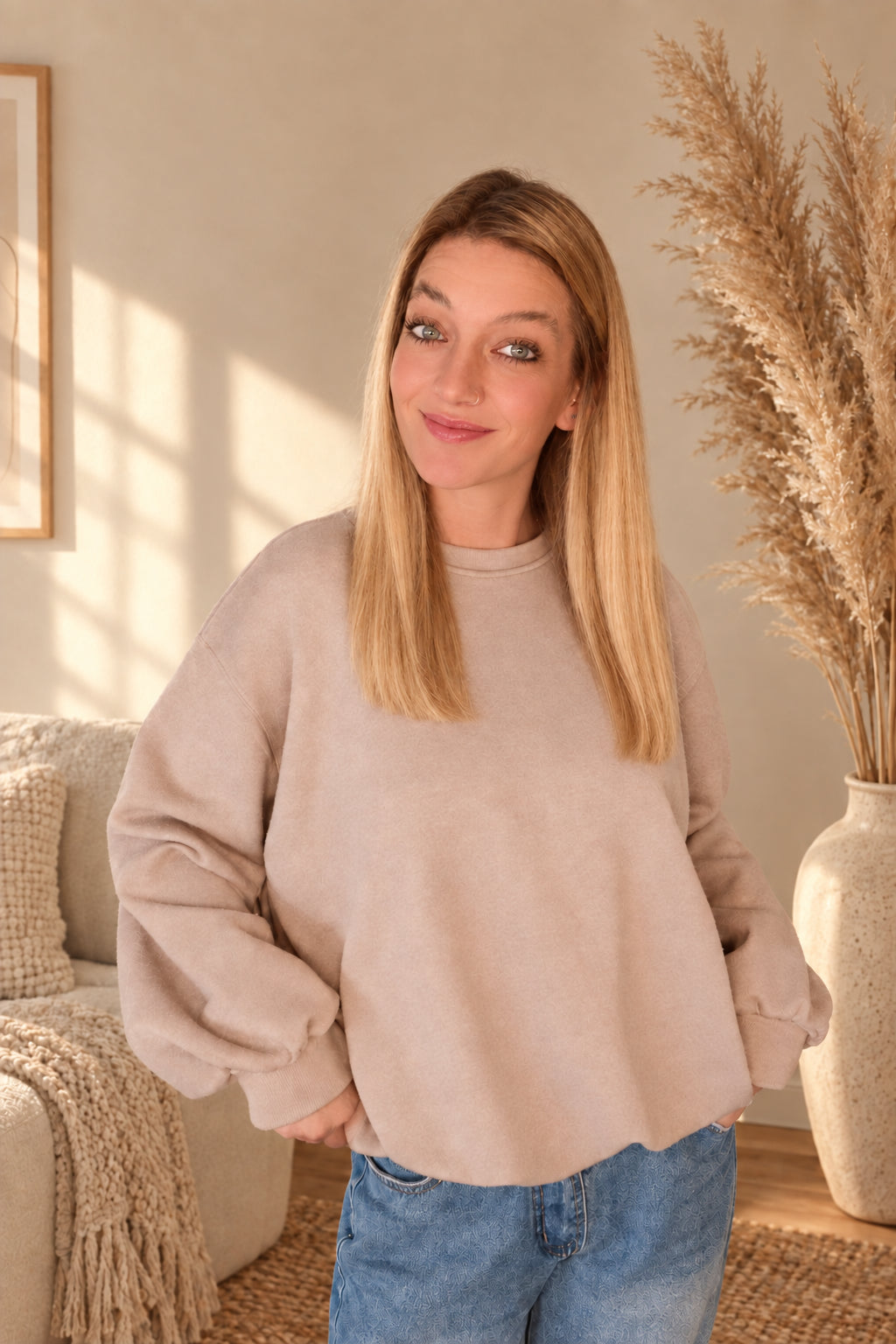 Beiges Damen-Sweatshirt mit voluminösen Ärmeln und Bündchen, Model hält den seitlichen Saum.