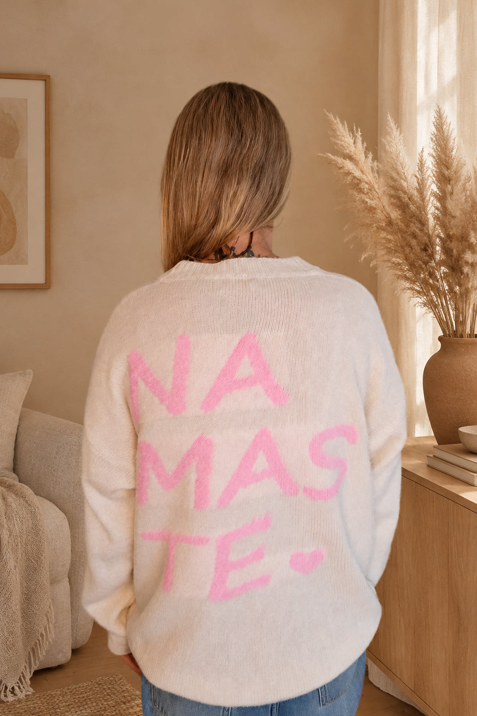 Cremeweißer Damen-Strickpullover von hinten mit großem rosa Namasté-Print, am Model mit gesenkten Armen.