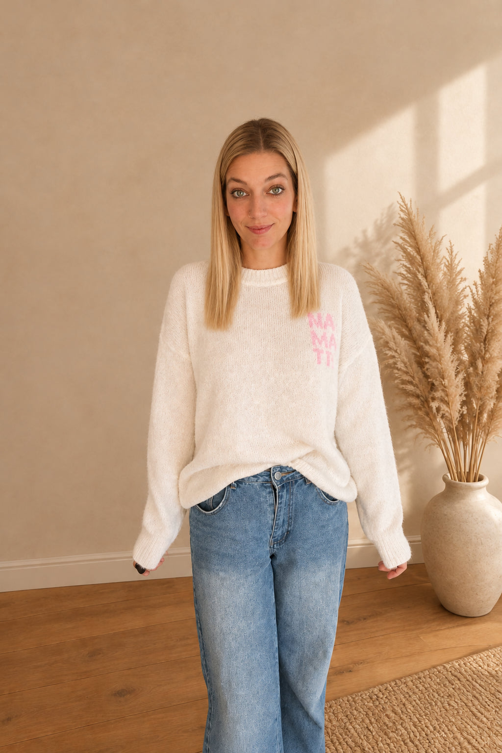 Vorderansicht des cremeweißen Damenpullovers mit rosa Namasté-Print, vorne locker in eine blaue Jeans gesteckt.