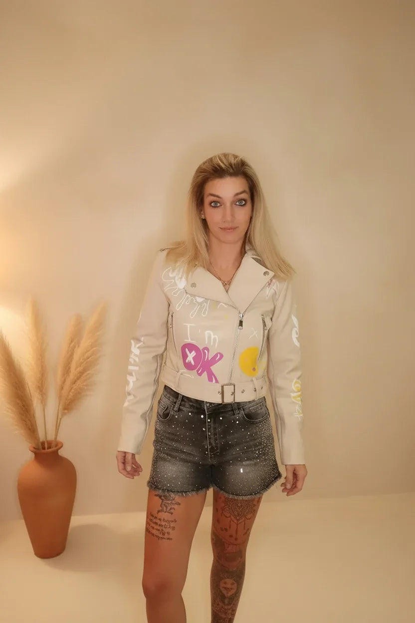 Frau in beige Lederjacke mit bunten Prints und dunklen Denim-Shorts im Boho-Luxe Stil.