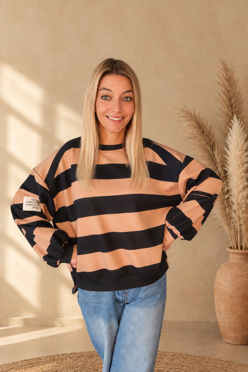 Damen-Sweatshirt mit breiten Streifen in Camel und Schwarz, am Model mit Händen an den Hüften und blauer Jeans.