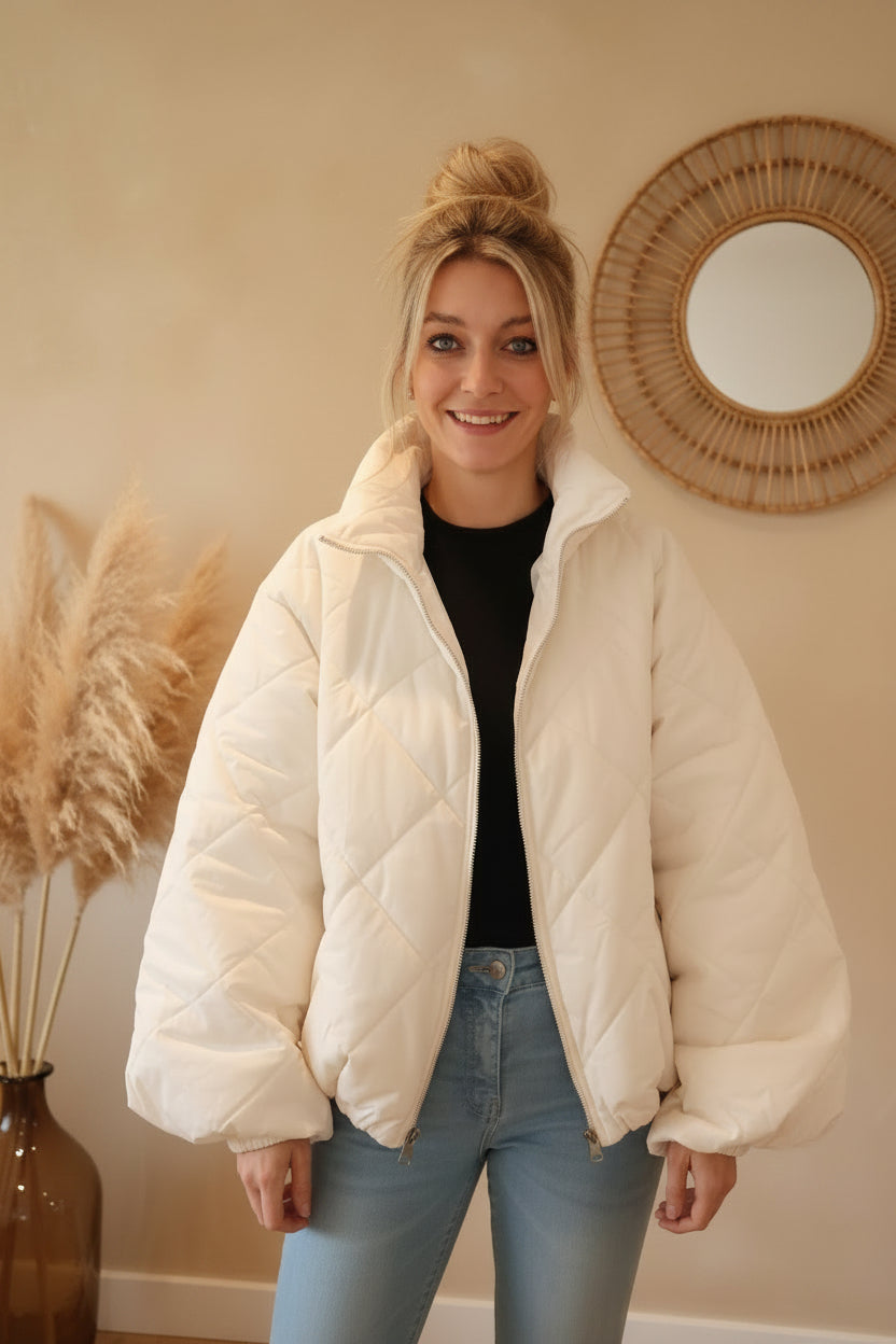 Frau in cremeweißer Steppjacke aus glattem Material im Boho-Luxe Stil mit hellblauen Jeans.