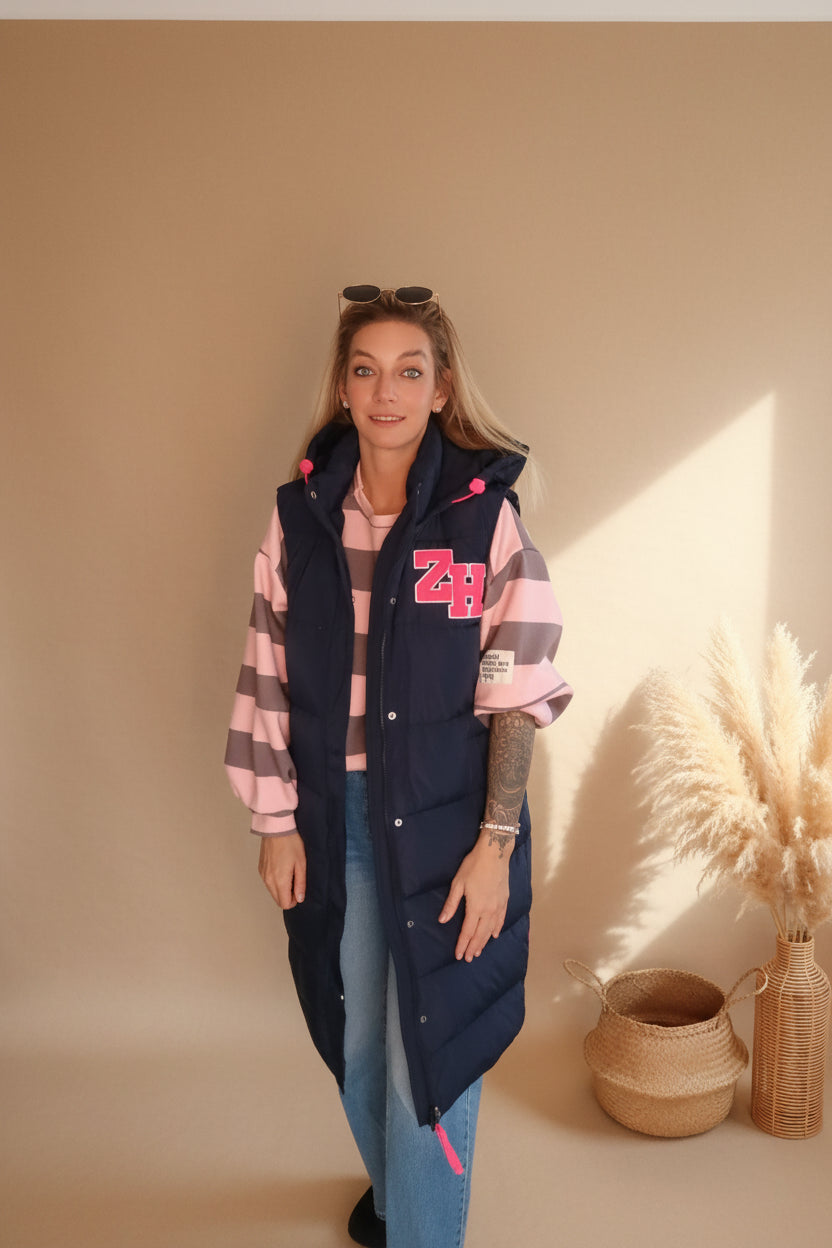 Frau in Boho-Luxe Look mit dunkelblauer Steppweste und rosa-grau gestreiftem Oberteil.