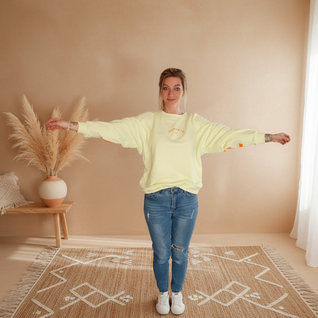 Namasté Oversize Sweatshirt Damen Pastellgelb – Frontansicht lässige Pose Hände in Hüften Neonorange Ärmel- und Frontprint Pampagras