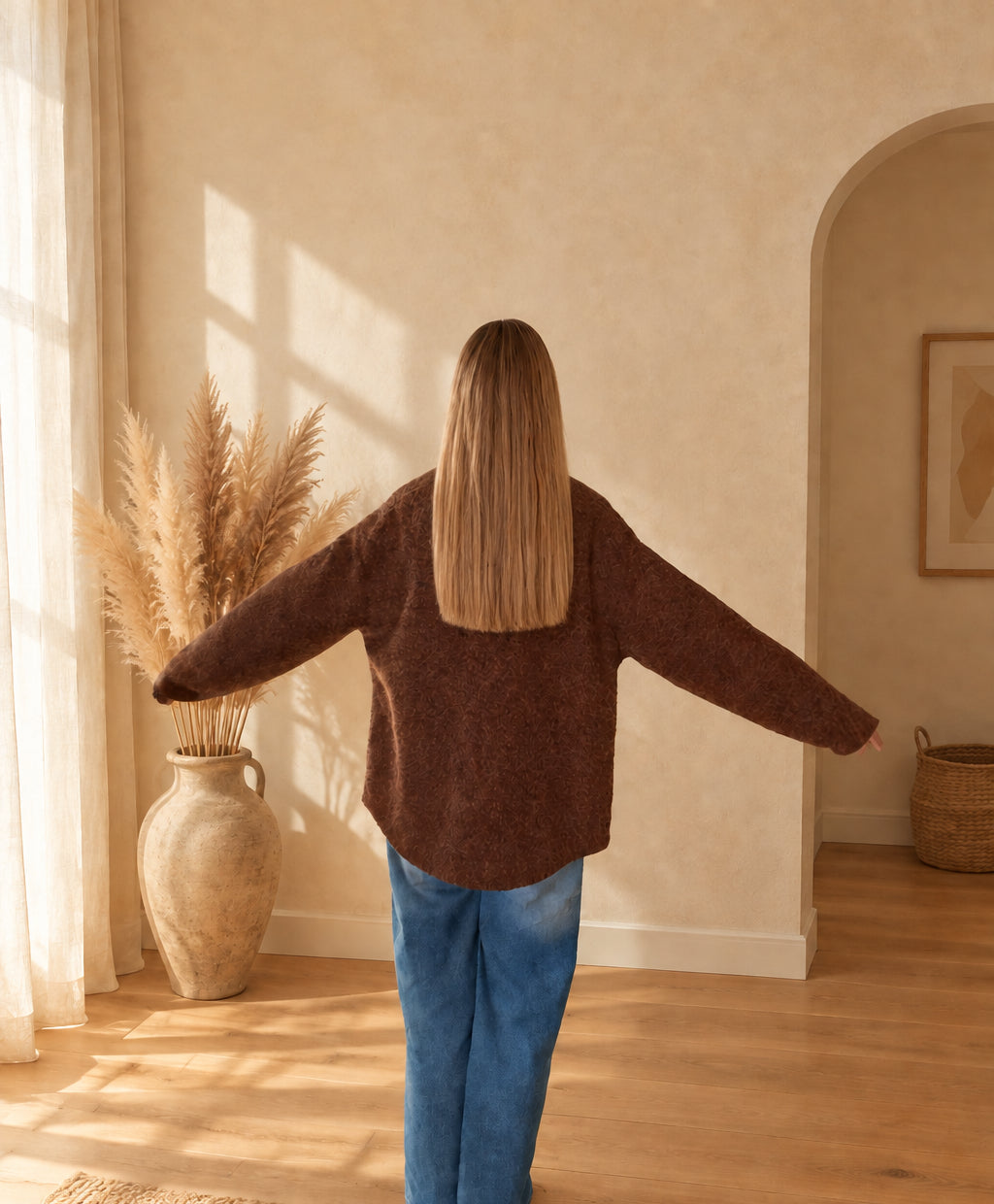 Rückansicht der braunen Damenjacke mit lockerem Schnitt und langen Ärmeln, am Model mit ausgestreckten Armen.