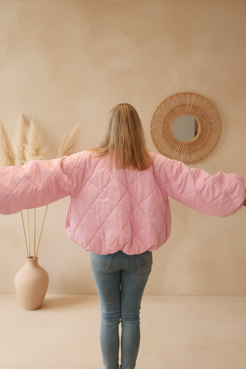 Frau in rosa gesteppter Boho-Luxe Jacke und blauen Jeans vor beigem Hintergrund