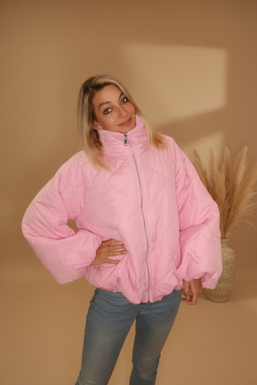Frau in einer rosa gesteppten Boho-Luxe Jacke aus glänzendem Material und Jeans