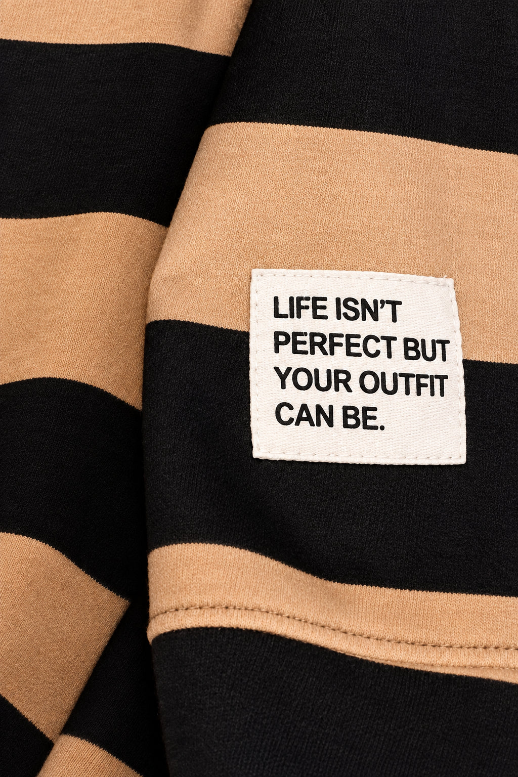 Nahaufnahme des Patches „Life isn’t perfect but your outfit can be.“ auf dem camel-schwarz gestreiften Sweatshirt.