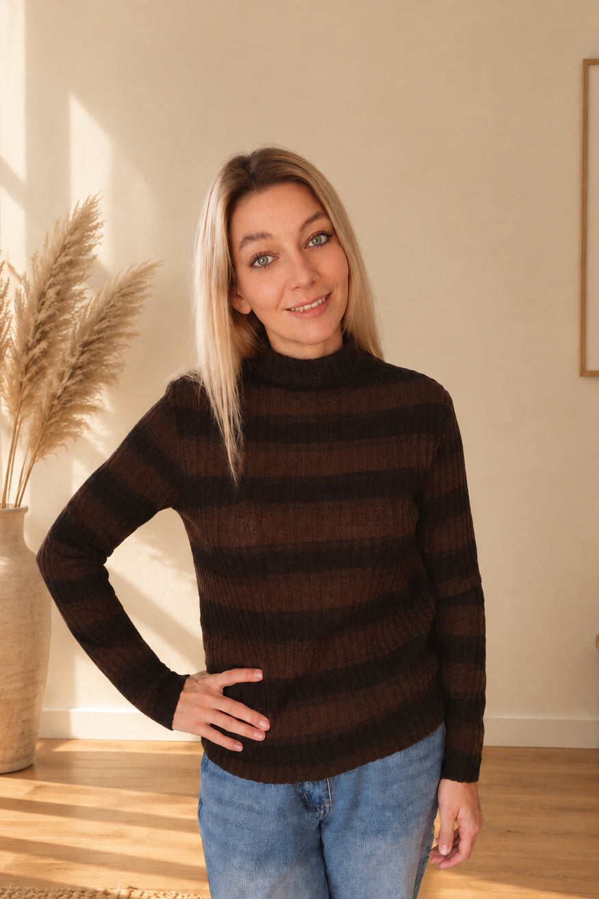 Gestreifter Damen-Strickpullover in Dunkelbraun-Schwarz mit hohem Kragen, am Model mit einer Hand an der Hüfte.
