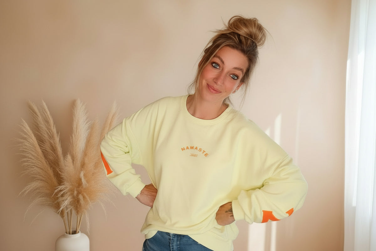 Namasté Oversize Sweatshirt Damen Pastellgelb – Oberkörper Nahaufnahme Hände in Hüften Namasté Frontprint Neonorange Ärmelprint