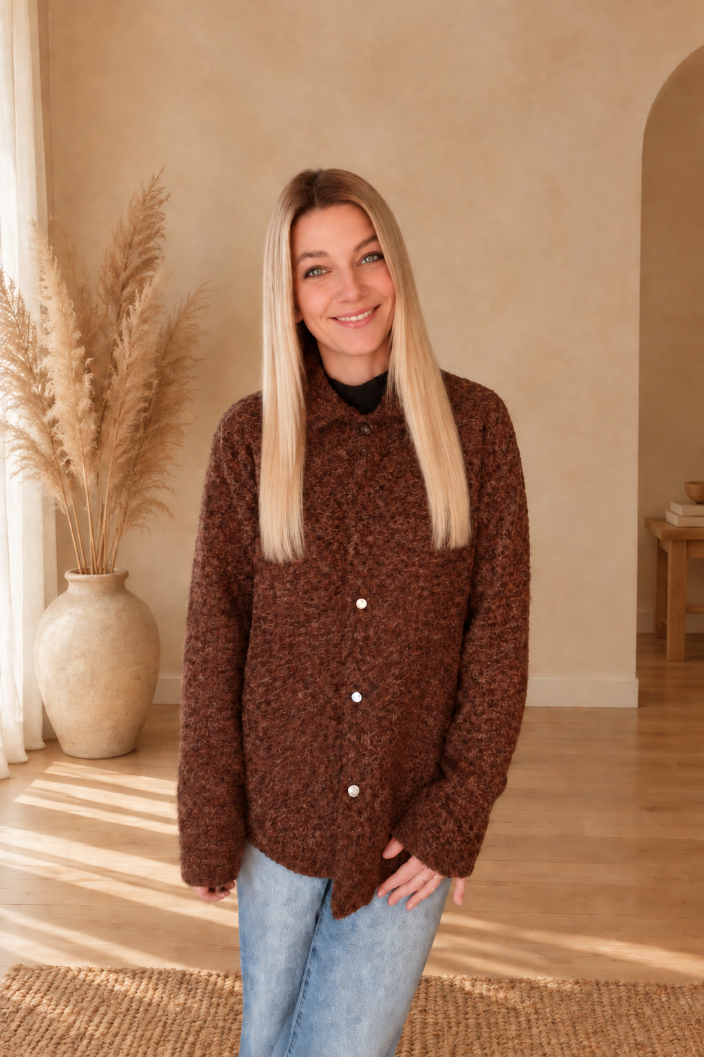 Braune Damenjacke mit strukturierter Oberfläche und heller Knopfleiste, geschlossen zur blauen Jeans getragen.