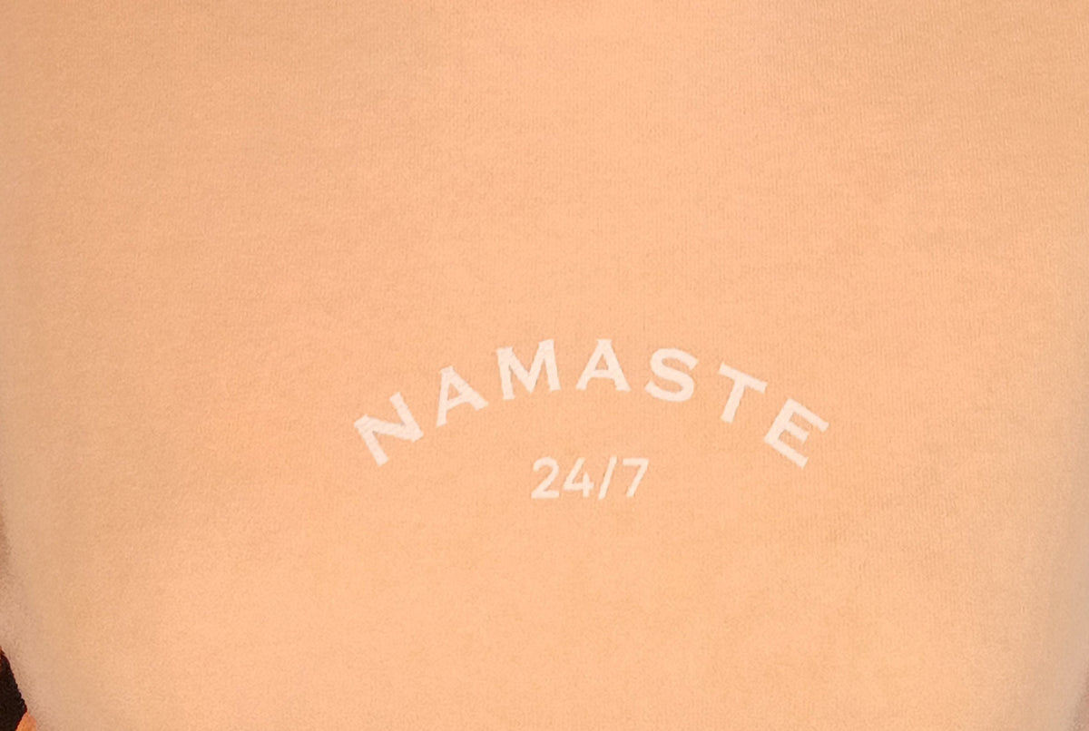 Detailaufnahme des weißen NAMASTE 24/7-Prints auf peachfarbenem Damen Sweatshirt