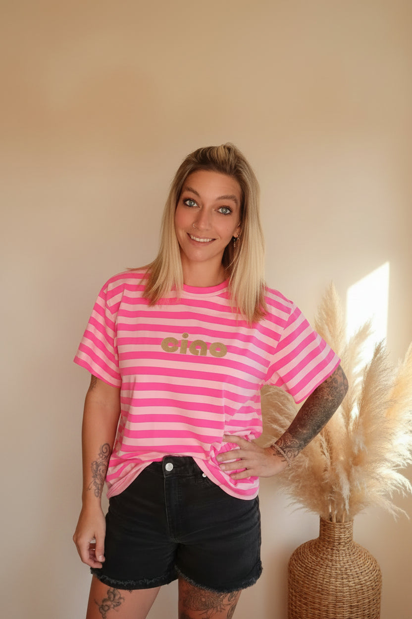 Frau in rosa gestreiftem T-Shirt und schwarzen Shorts vor hellem Hintergrund.