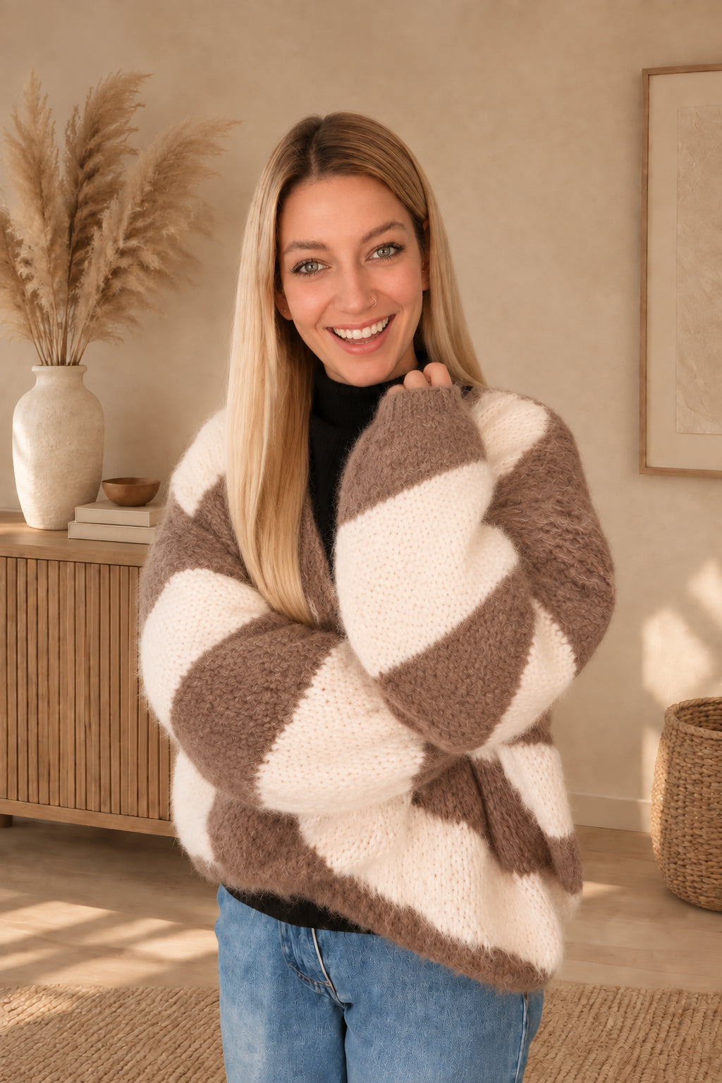 Nahansicht der Strickstruktur und weiten Ärmel des taupe-creme gestreiften Cardigans, am Model mit verschränkten Armen.