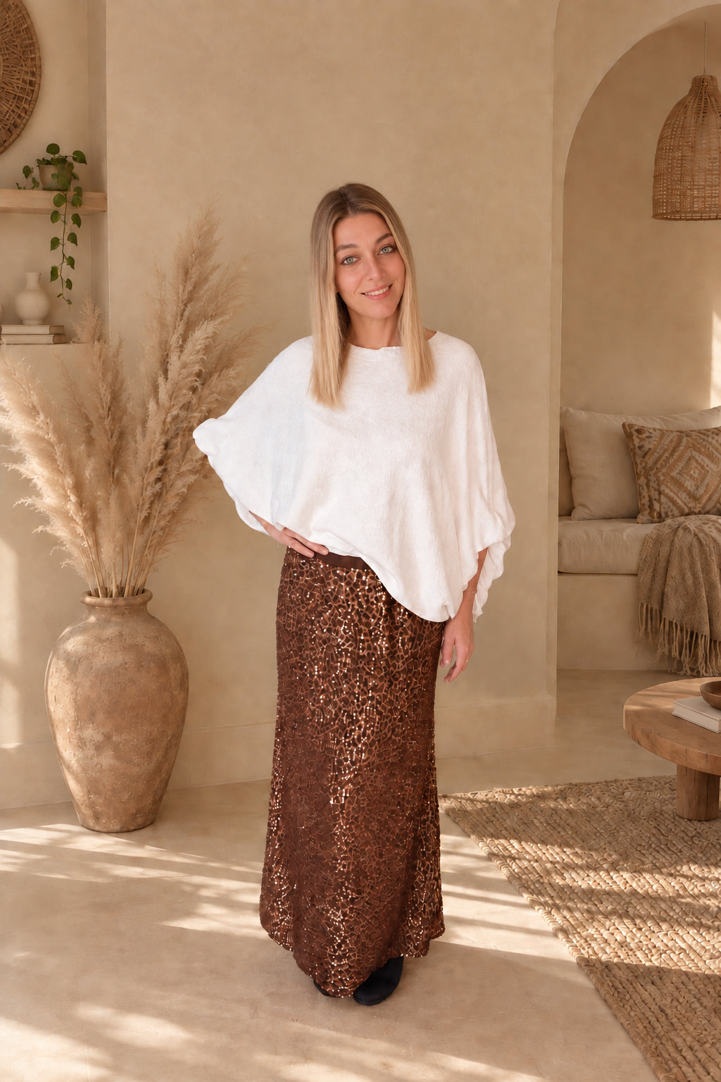 Frau im Pailletten-Maxirock Leo Bronze lächelnd, Frontansicht mit weißem Poncho-Pullover