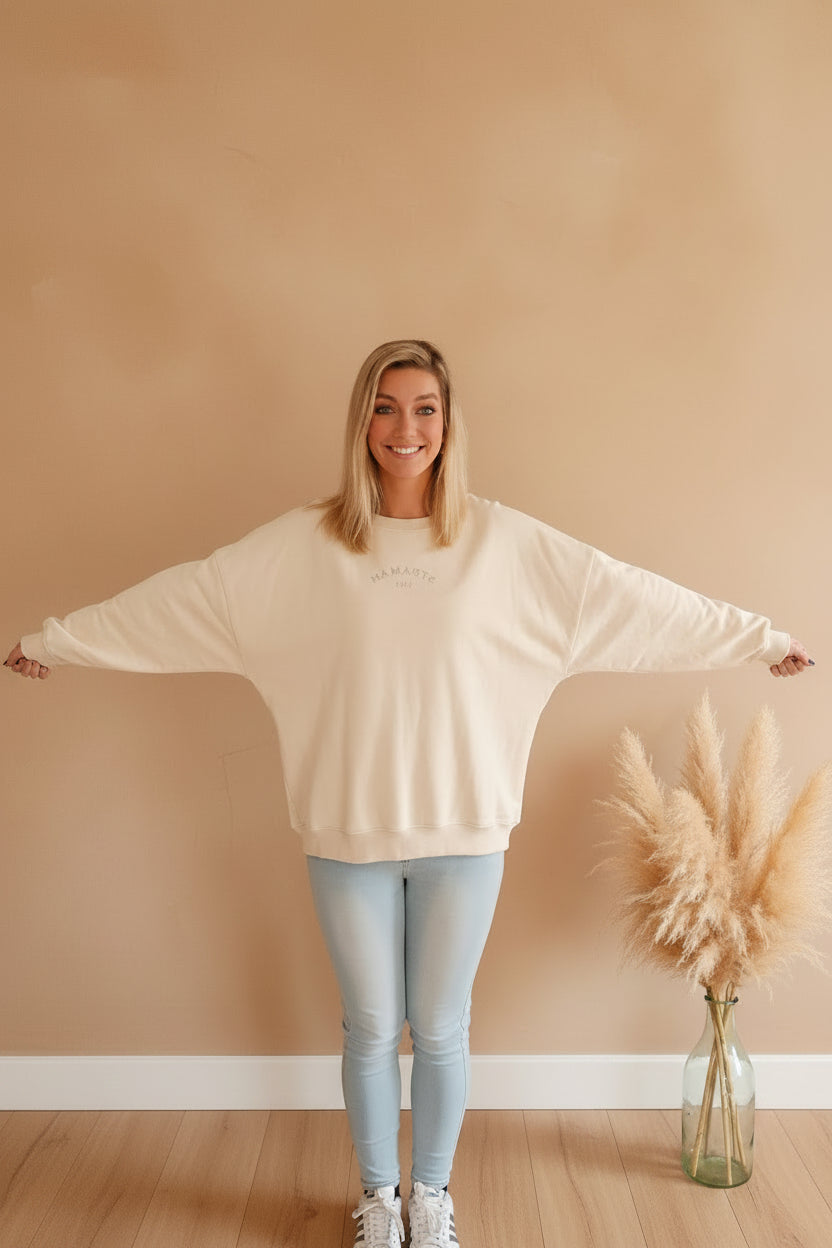 Namaste 24/7 Oversized Sweatshirt Creme – Oversized Fit, Arme ausgebreitet, Makramee-Deko im Hintergrund