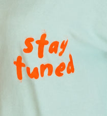 Detailaufnahme des orangefarbenen Stay-tuned-Prints auf mintfarbenem Damenpullover