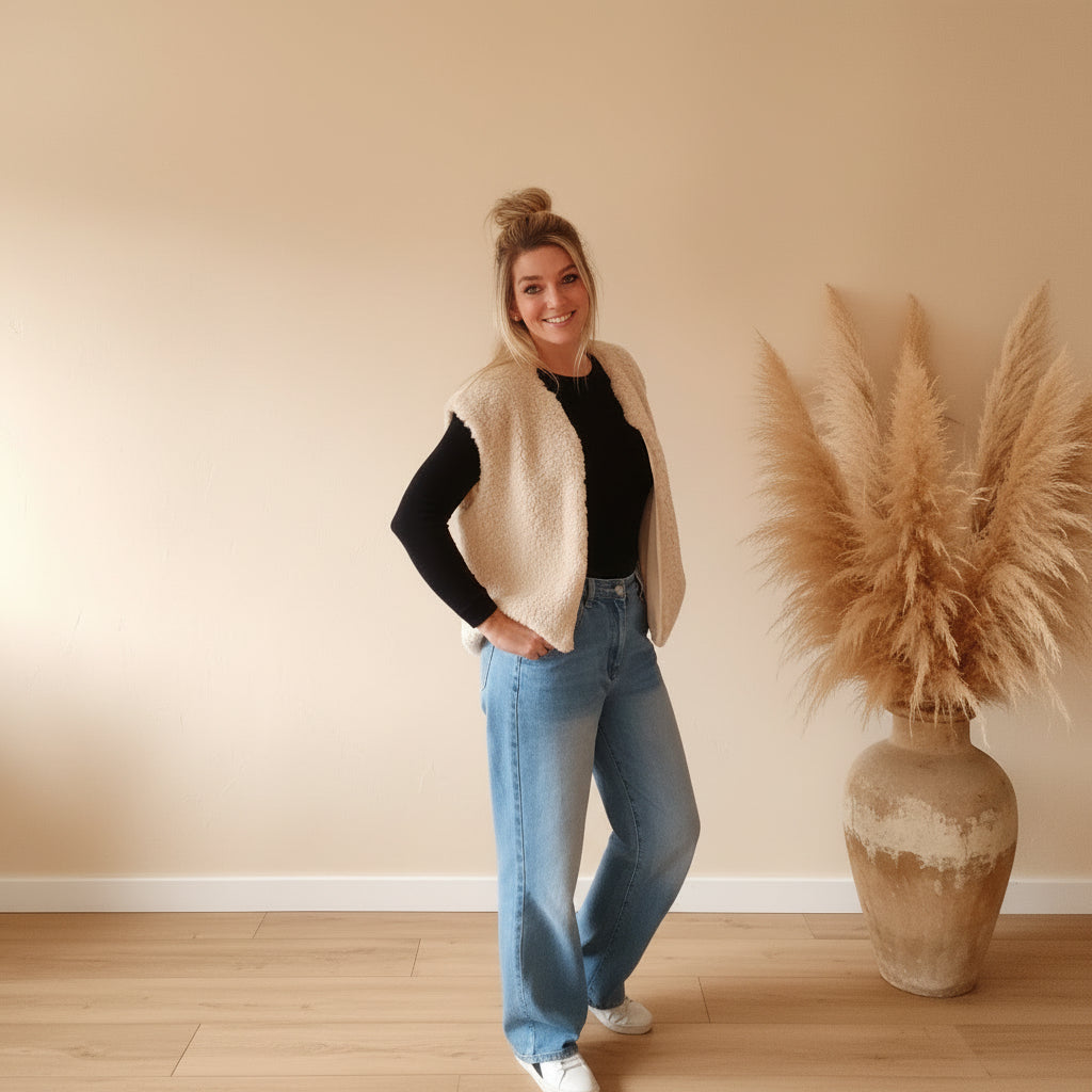 Cremefarbene Teddyfell-Weste für Damen in seitlicher Frontansicht, offen getragen mit Jeans und weißen Sneakern
