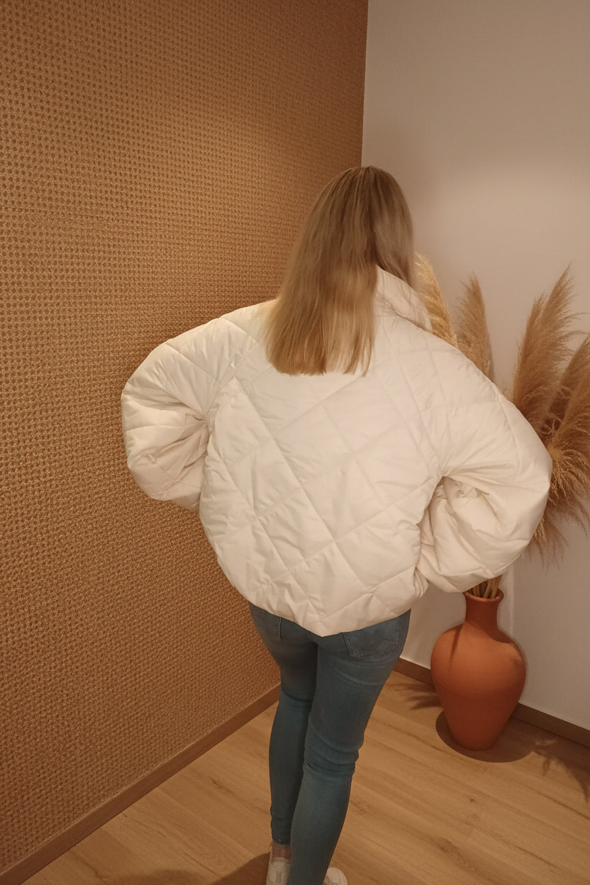 Rückansicht einer Frau in einer weißen, gesteppten Boho-Luxe Jacke und blauen Jeans.