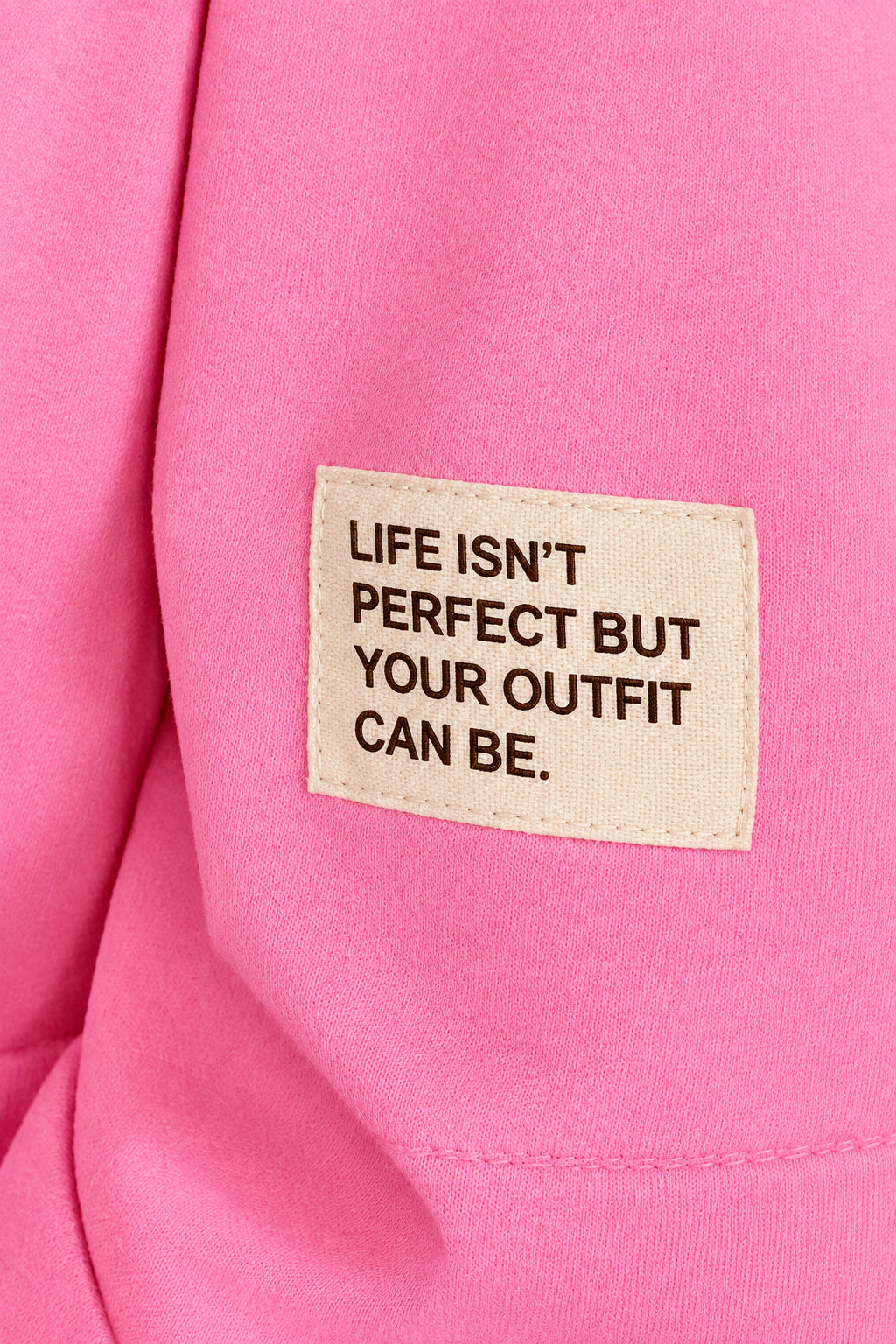 Nahaufnahme des hellen Ärmelpatches auf pinkem Stoff mit der Aufschrift „Life isn’t perfect but your outfit can be“.
