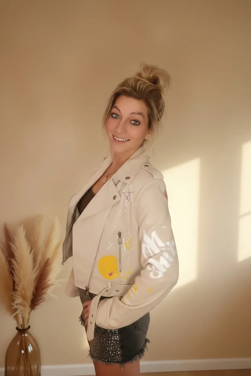 Frau in beiger Lederjacke mit Graffiti-Prints und grauem Minirock im Boho-Luxe Stil.