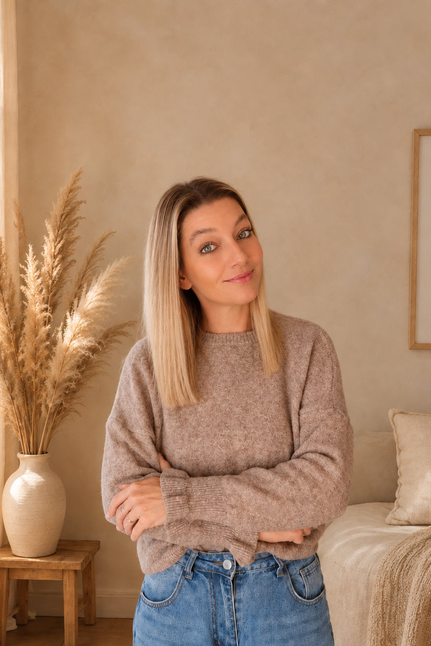 Model trägt einen taupefarbenen Damenpullover zu Jeans, die Arme vor dem Körper verschränkt.