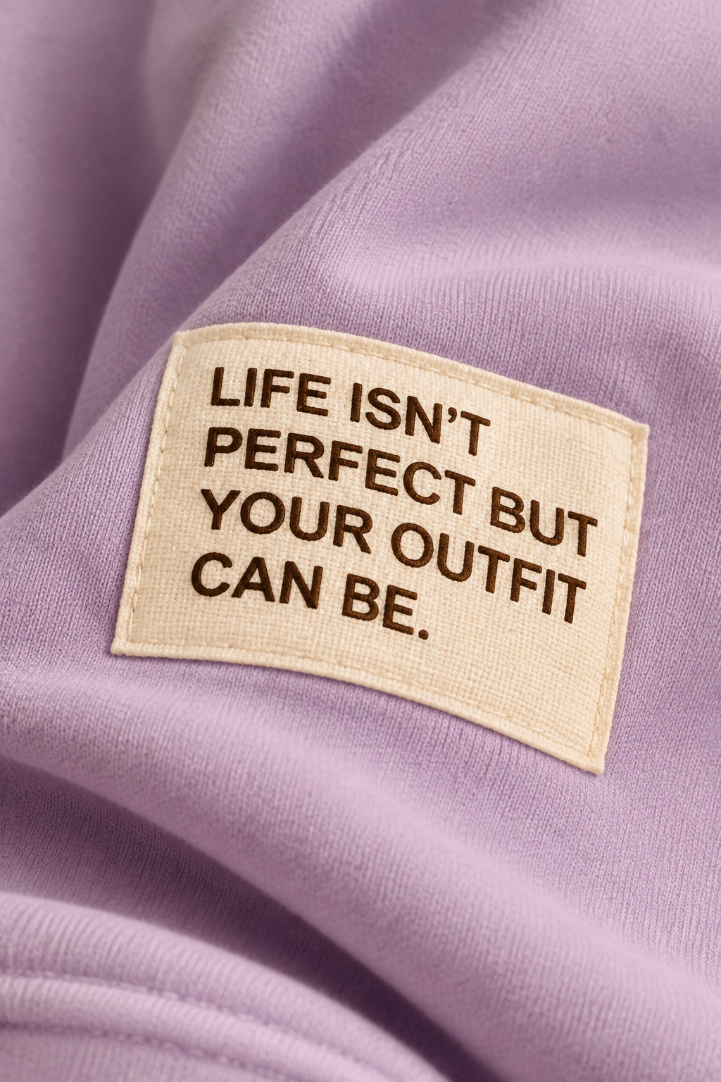 Nahaufnahme des hellen Ärmelpatches auf fliederfarbenem Stoff mit der Aufschrift „Life isn’t perfect but your outfit can be“.