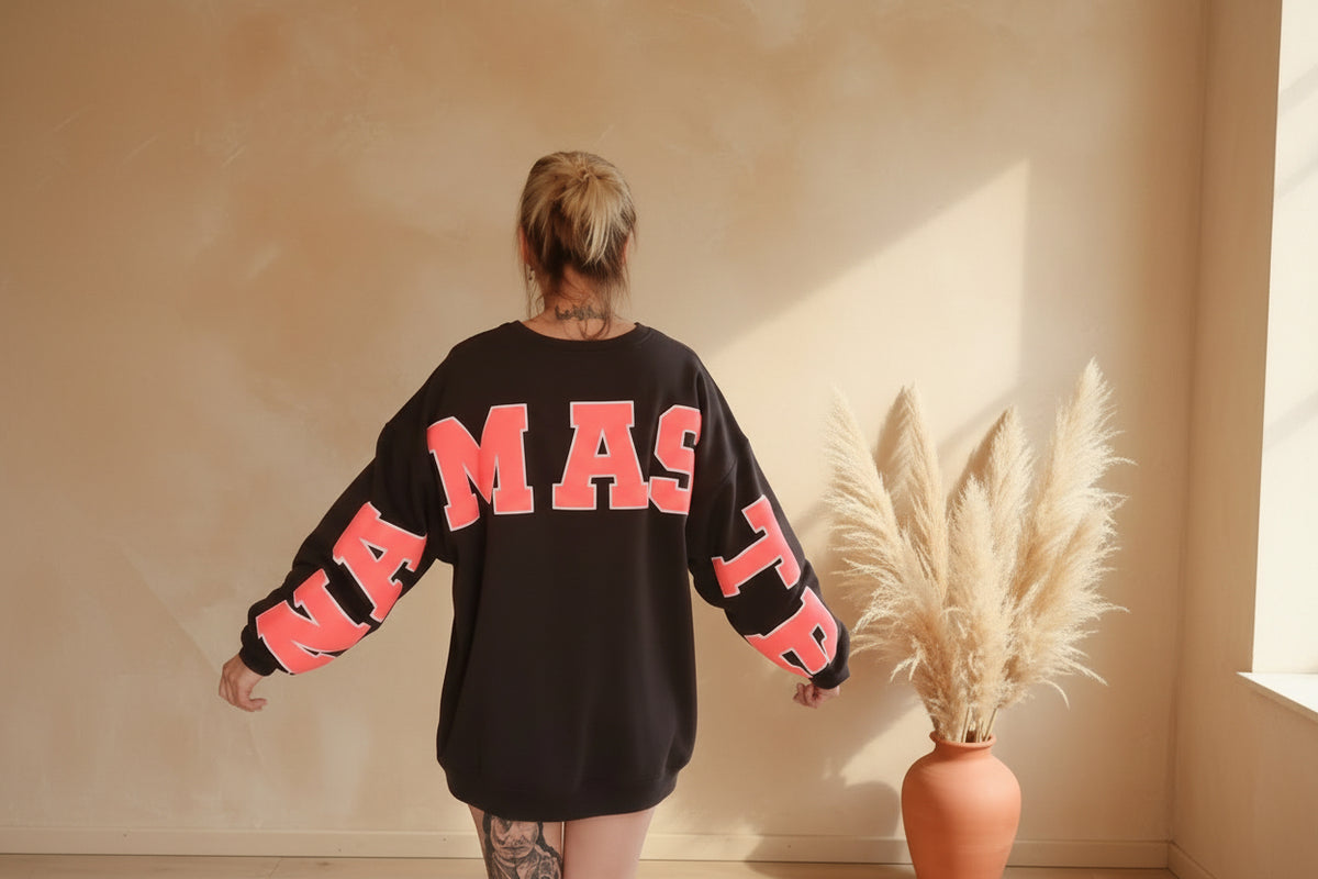 Schwarzer Oversize-Sweatshirt mit pinkem Namaste-Schriftzug im Boho-Luxe-Stil.