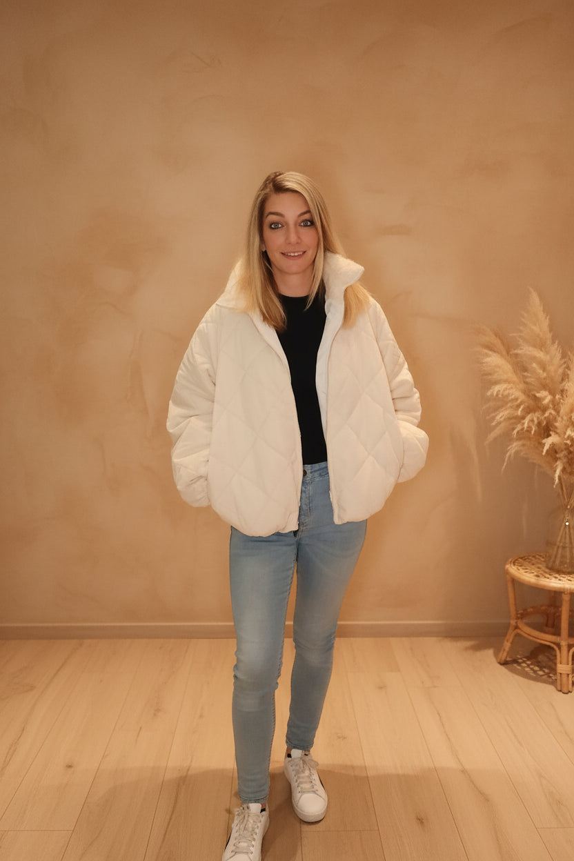 Frau in weißer gesteppter Steppjacke aus Polyestermaterial und hellblauen Jeans im Boho-Luxe-Stil.