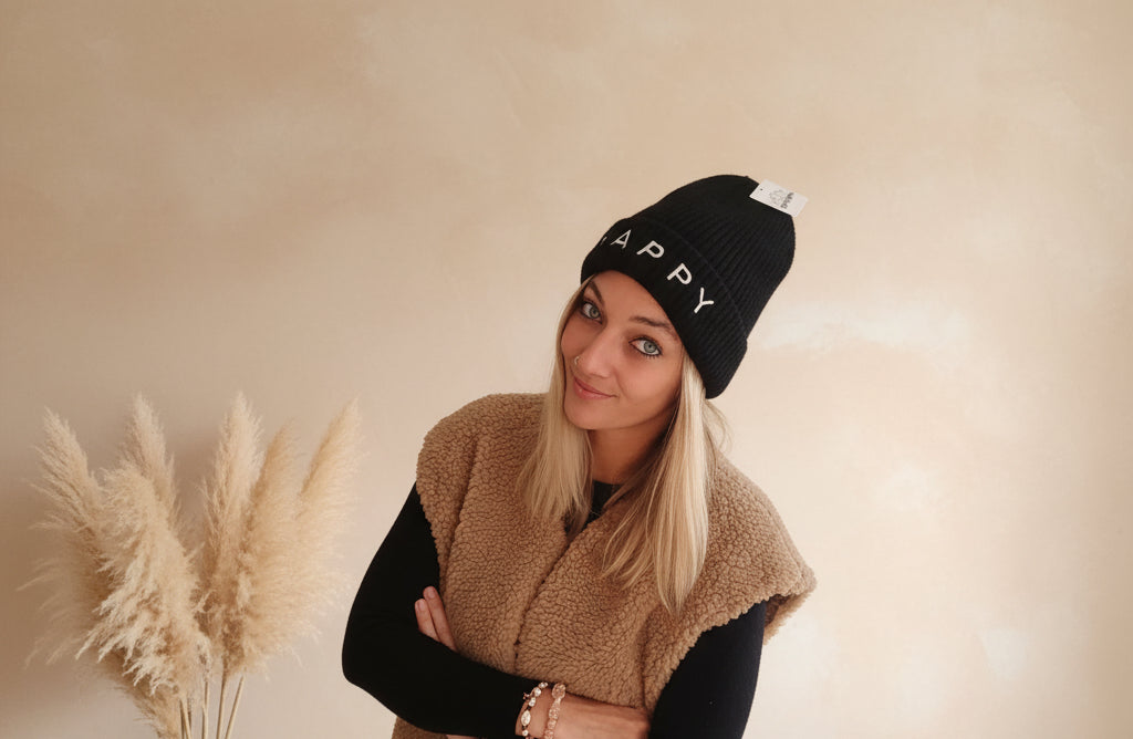 Schwarze HAPPY Strickmütze für Damen in Frontansicht, getragen mit schwarzem Outfit