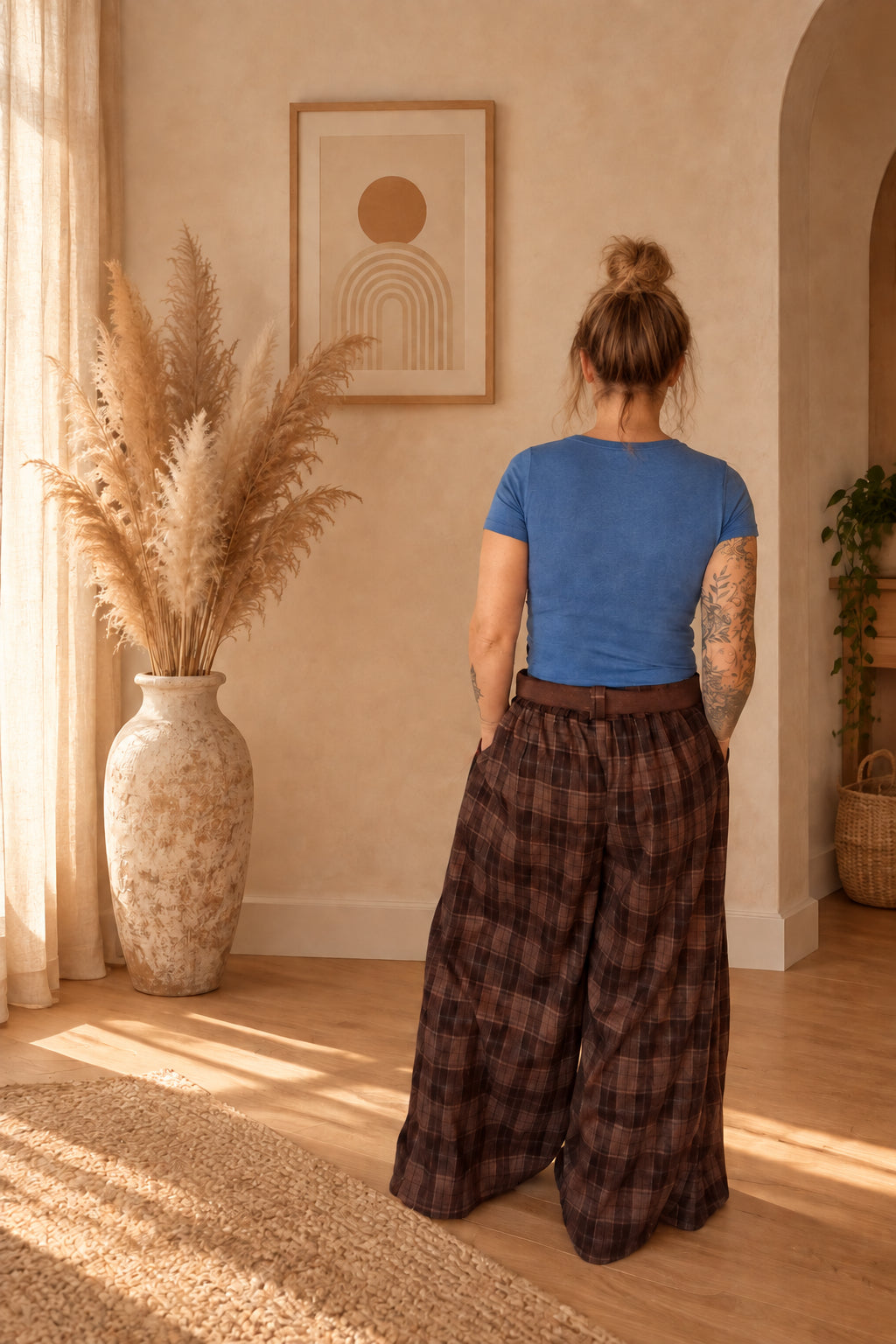 Rückenansicht der braunen karierten Damenhose mit weitem Bein und gerafftem Bund, am Model mit blauem T-Shirt