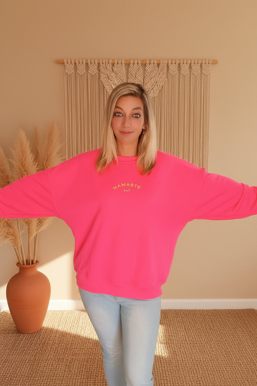 Namaste 24/7 Oversized Sweatshirt Pink – Oversized Fit, Arme ausgebreitet, Makramee-Deko im Hintergrund
