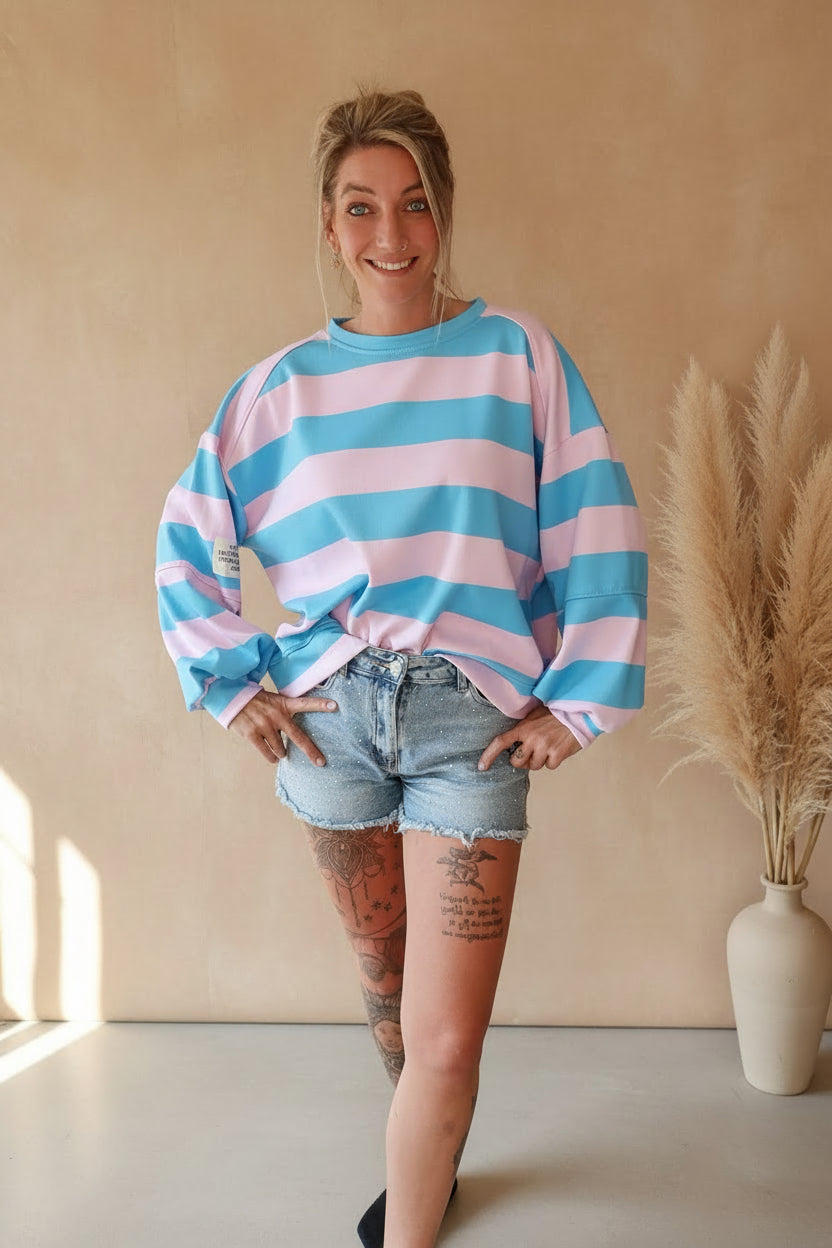Boho-Luxe Look: Gestreifter Oversize-Sweatshirt in Rosa und Blau mit hellblauen Jeans-Shorts.